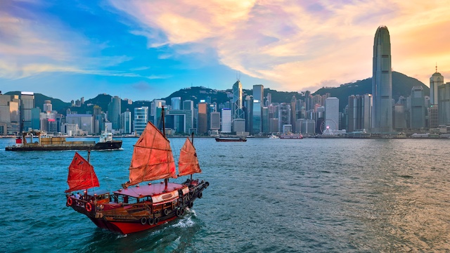 Hong Kong skyline cityscape downtown skyscrapers over Victoria Harbour in the evening with junk tourist ferry boat on sunset with dramatic sky. Hong Kong, China
